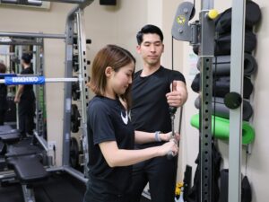 トレーニングマシンの前で、トレーナーが女性のお客様にフォームを指導している様子