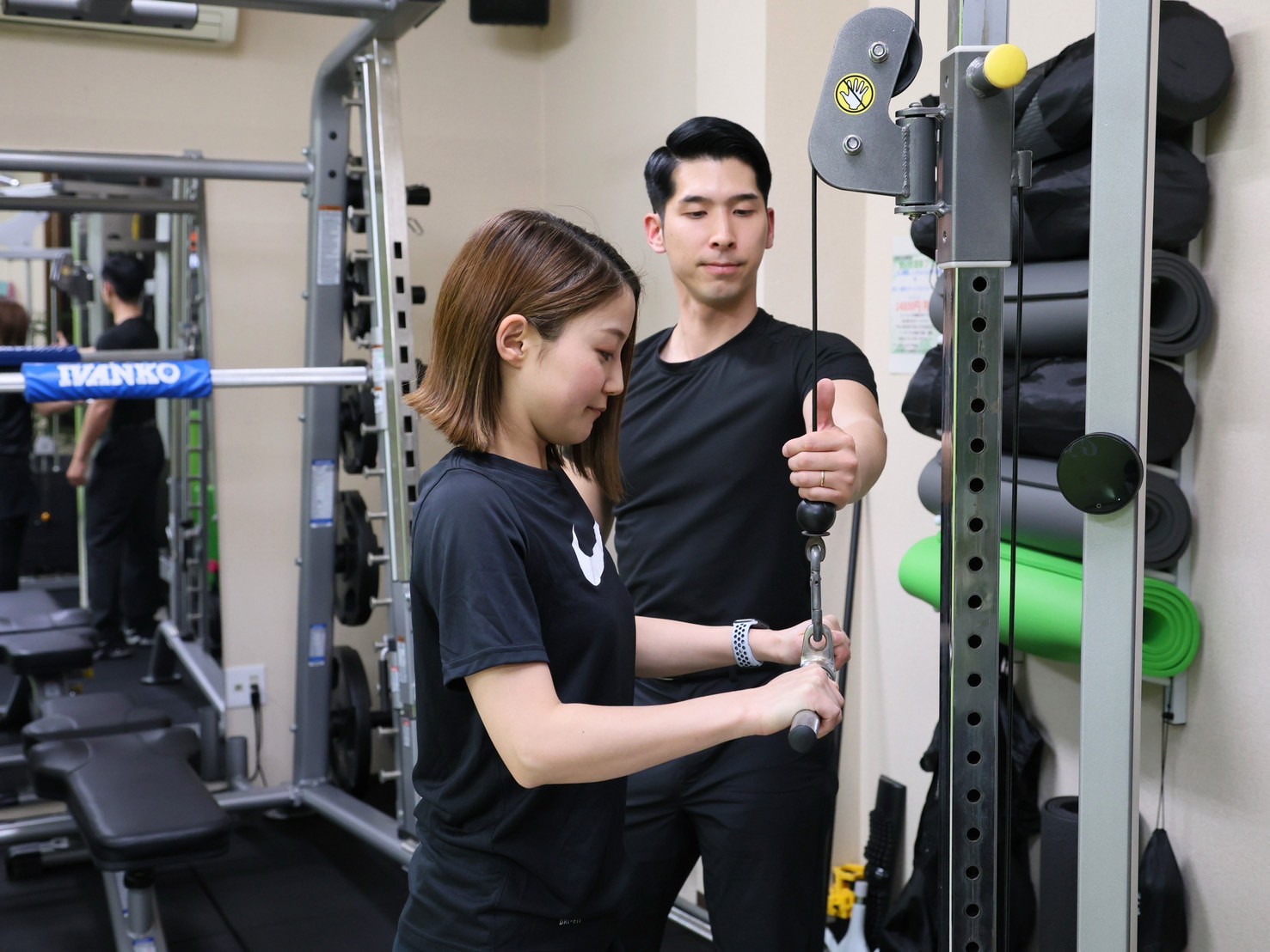 トレーニングマシンの前で、トレーナーが女性のお客様にフォームを指導している様子